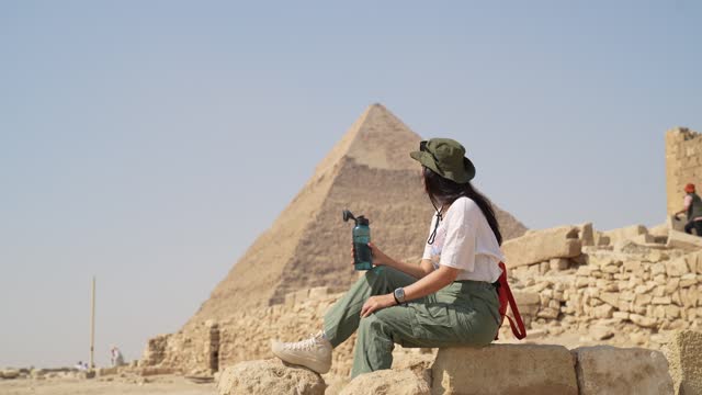 Egypt, Cairo, asian woman tourist sitting  on rocks with Great Pyramid of Giza in background