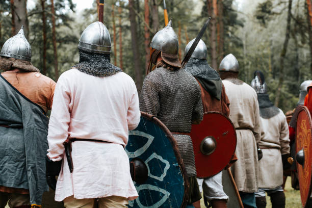 istock Back view of group of ancient warriors in chain mail, helmets with weapons standing in forest, costumed medieval festival outdoors 1686629507