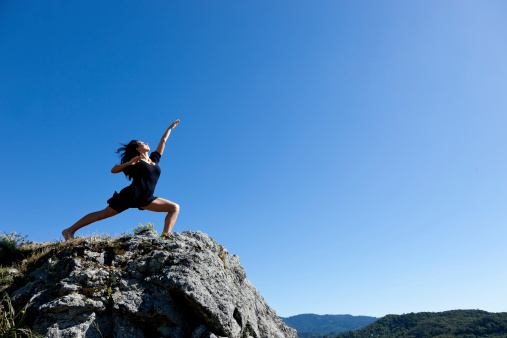 modern female dancer striking a dance pose on top of a mountain with clear blue sky in background