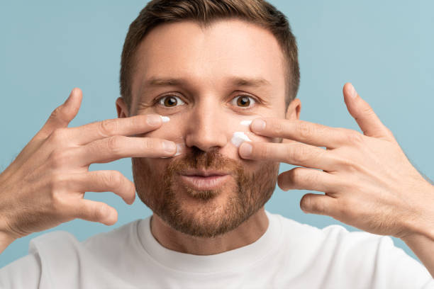 istock Young man having fun applying face cream on cheeks two hands looking at camera smiling closeup 1686659719