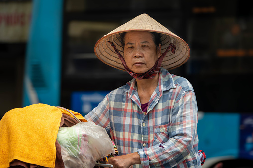 Woman with a conic straw hat pushing a bicycle in the streets of Hanoi, Vietnam. Close-up.