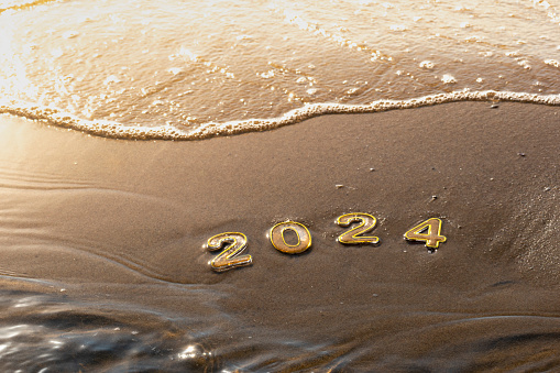 New year 2024 background. 2024 numbers on wet golden sand of beach in sun rays light and rolling sea wave. Celebration New Year's Eve holidays at seaside resort, travel, change, new beginning, vision