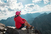 Trekker woman dressed red active people clothes sitting on Rysy peak 2499m enjoying High Tatras mountain range covered mist, clouds with incredible light and shadows. Nature trekking, climbing concept