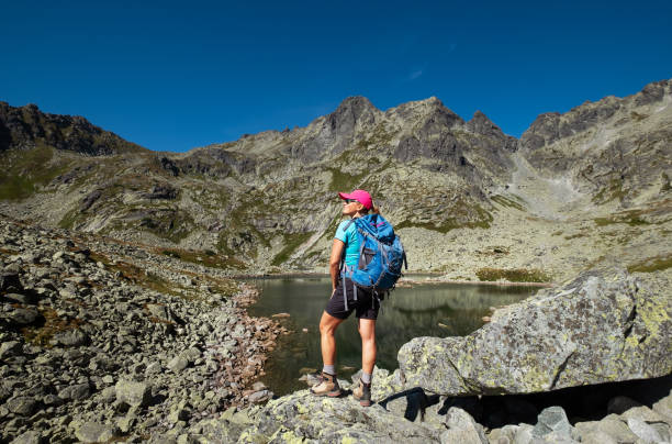 Trekker woman near Velke Zabie pleso mountain lake (Tarn) 1919m enjoying High Tatras mountain range with Rysy 2499m peak. Active people, nature trekking, climbing activities concept. Trekker woman near Velke Zabie pleso mountain lake (Tarn) 1919m enjoying High Tatras mountain range with Rysy 2499m peak. Active people, nature trekking, climbing activities concept. tatra tourists stock pictures, royalty-free photos & images