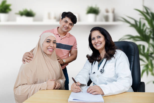 Portrait of Indian female doctor consulting young muslim married couple patients in fertility clinic about IVF or IUI. Planning pregnancy concept. Smiling looking at camera Portrait of Indian female doctor consulting young muslim married couple patients in fertility clinic about IVF or IUI. Planning pregnancy concept. Smiling looking at camera wafid medical appointment = stock pictures, royalty-free photos & images