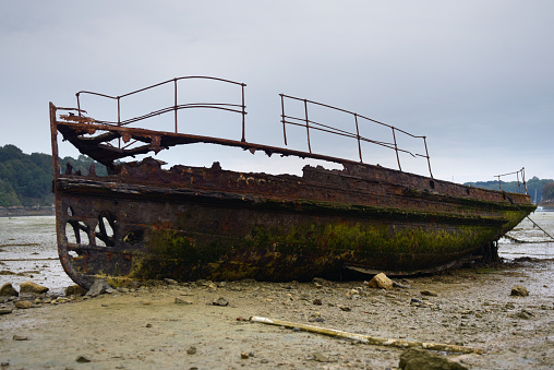 A side view of an old rusty vessel that is being taken apart.