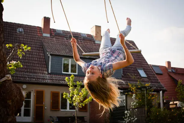 rear view of Girl on a swing in the back yard in front of a small house