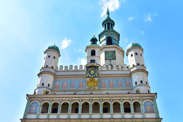 View of the facade of the town hall with columns, blue walls with frescoes, golden clocks and steeple. Bottom-up view. Central square. Poland, Poznan, July 2022.