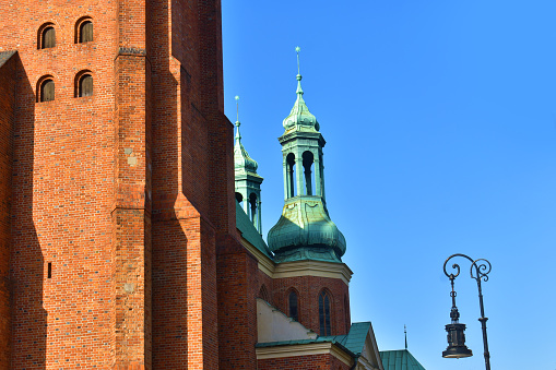 Cathedral towers with a green top and red brick's wall of catholic church, in the background of blue sky. A sunny summer day. Cathedral on the Tymsky island. Poland, Poznan, June 2022.