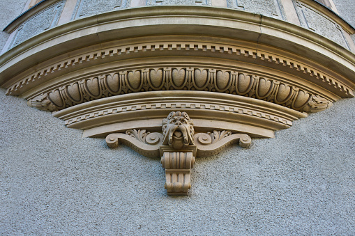 Architectural decorative element on the wall in the form of upward diverging bands of ornament and with a sculpture of a head at the base. Stone form. Ancient building. Poznan, Poland, September 2022.