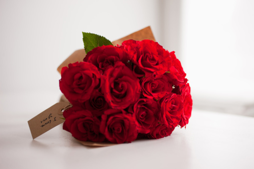 Beautiful red rose bouquet on woman hand, woman holding and showing red rose to camera while standing in decorative room. Romantic girl with flower for celebrating love on Valentine Day.