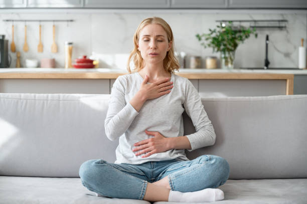 Woman doing calming breathing exercises after panic attack Concept of mental health. Woman sitting on couch and doing calming breathing exercises after panic attack. Female inhaling and exhaling to deep breath. Self-control, anxiety relief concept woman breathing deep stock pictures, royalty-free photos & images