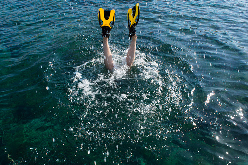 Woman with yellow flippers diving under the blue sea water, splashing