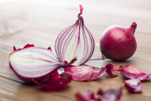 Several natural raw red onions. Some sliced in half. Among the peelings. On a wooden table.