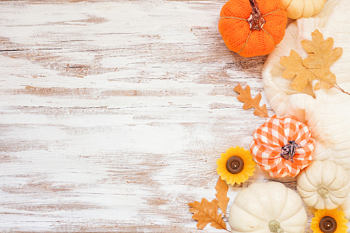 Autumn country farmhouse side border over a white wood background. Orange and white cloth pumpkins, sweater, candles and fall leaves. Top down view with copy space.