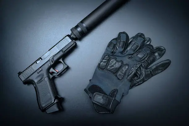Pistol with silencer and gloves on the black background, close up photo