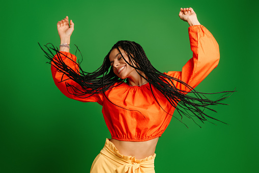 Joyful young woman with dreadlocs dancing and smiling against green background
