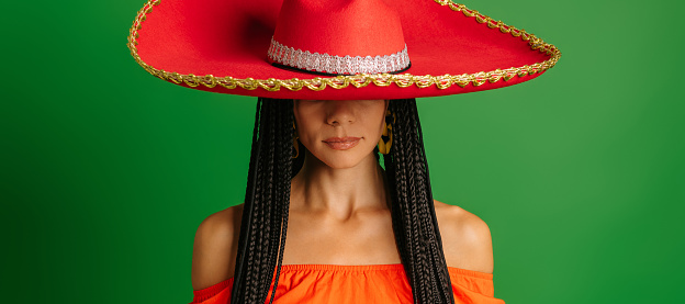 Gorgeous young Mexican woman in Sombrero standing against green background