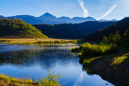 Scenic Mountains and Lake Reflections - Summer morning with rugged peaks rising up into the sky and calm lake with mist rising from surface. Sawatch Mountain Range, Colorado USA.