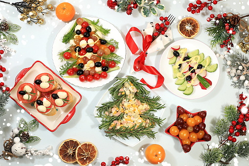 Christmas New Year dishes 2024, traditional holiday salads in the form of fir trees and fetax with tomatoes, olives and cheese, decorated with fir branches, cones and decorations, dish design idea, cafe menu, selective focus,