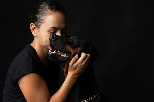 Side view of caucasian female  and hugging Doberman pinscher dog  on black background.