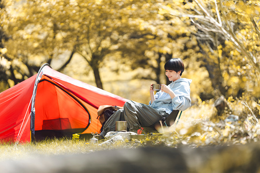 Young Asian woman is doing solo camping and drinking.
