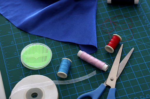 Hands of tailor with thread and needle sewing two parts of clothing