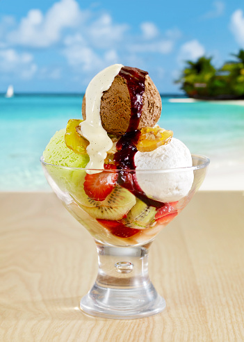 Cup of ice cream with fresh fruits on table at a tropical beach