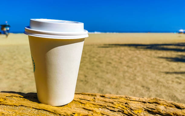 istock Coffee to go mug on the beach sand sea waves. 1687080719