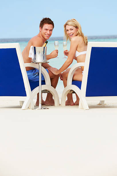 пара на пляж, отдыхая в кресле и пить шампанское - male swimwear cooler 20s стоковые фото и изображе�ния