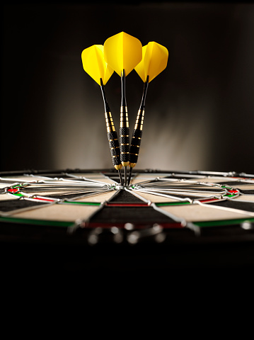 Three yellow darts hitting the target in a game of darts scoring a bulls eye. Copy space
