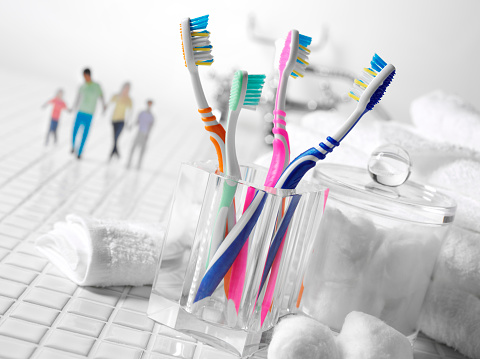 Family dental hygiene with adult and children's toothbrushes, cotton wool and soft white towels. Family in the background on a tiles bathroom floor.