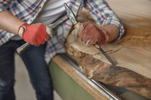 Carpenter in glasses working with chisel while cutting wooden plank in carpentry workshop