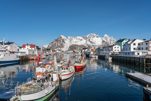 Port of fishing village Henningsvær in the Lofoten Island. Lots of fishing boats on sunny winter day against rocky mountain.