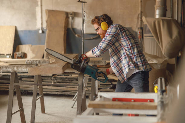 istock Professional carpenter in glasses is cutting wood with chainsaw on carpentry workshop 1687157880