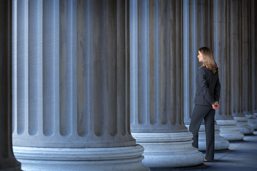 A female lawyer, banker, or businesswoman standing among large columns looking out into the distance.