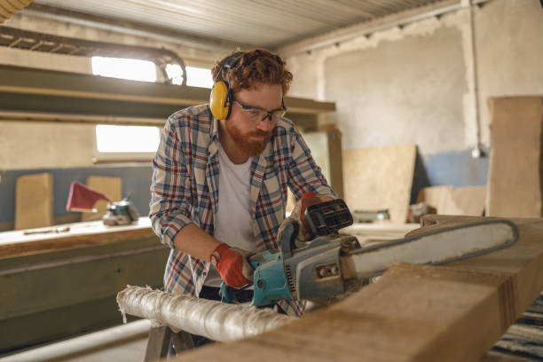 istock Professional carpenter in glasses is cutting wood with chainsaw on carpentry workshop 1687158433