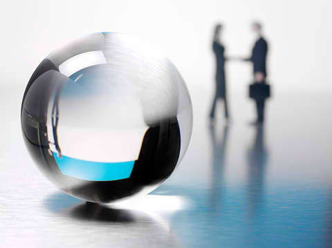 Crystal ball with business people shaking hands in the background. Differential focus. Copy space. 