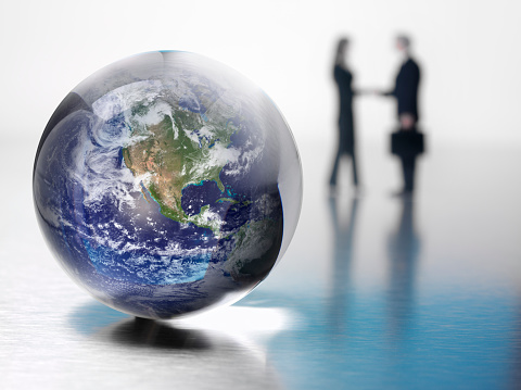 World map in a crystal ball with business people shaking hands in the background. Differential focus. Copy space