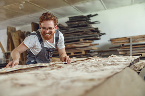 Smiling woodworker measures wooden planks in the carpentry workshop. High quality photo
