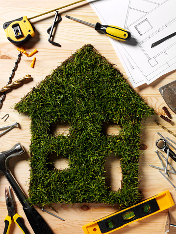 Grass house cut out with construction tools on a wooden background.