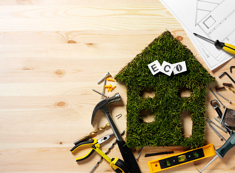 Eco house cut out of grass with construction tools on a wooden background. Copy space