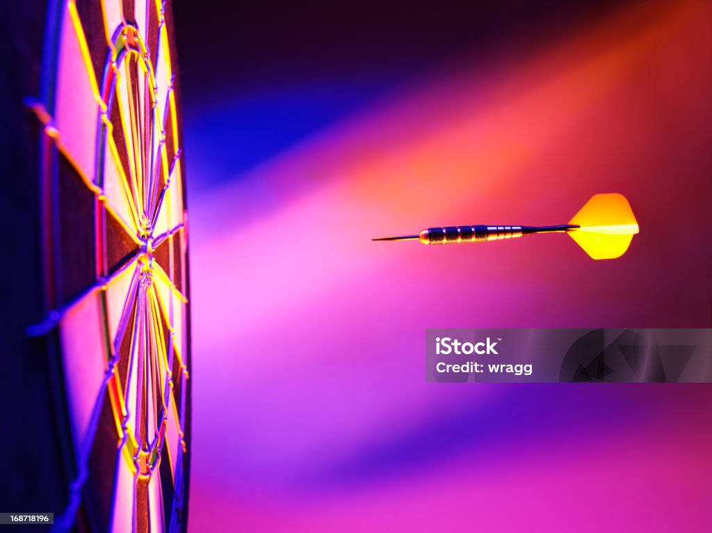 Yellow Dart Pink Lighting on a Dartboard One yellow dart hitting the target in a game of darts scoring a bulls eye. Pink and purple lighting with copy space. Darts Stock Photo