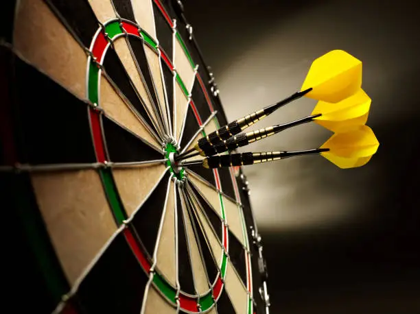 Three yellow darts hitting the target in a game of darts scoring a bulls eye. 