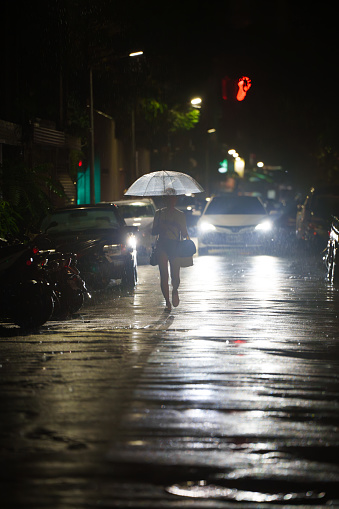 A woman walking alone with an umbrella in a dark alley on a rainy night and a car lighting it up, Taipei, Taiwan