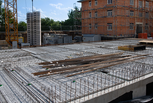 A construction site in Germany. The ceiling in the basement of an apartment building is cast in concrete. Iron bars protrude from the ceiling and lie on top. In the background is the shell of another house.