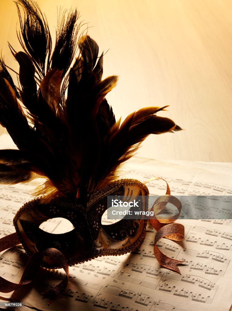Sheet Music and Masquerade Mask Feather masquerade mask on sheet music with copy space on a wooden table. Brown Stock Photo