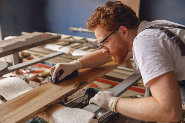 istock Professional carpenter coating a wooden board with protective oil in a workshop. High quality photo 1687204218