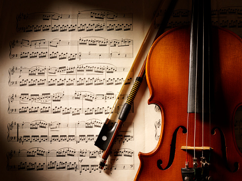 Wooden violin on sheet music with shadow.