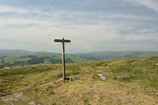 Wooden signpost showing the way on a high moorland path with rolling grassy hills in the background